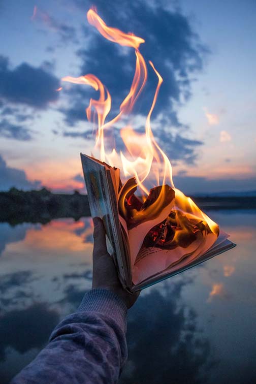 Hand holding book out that's on fire and burning, lake in background