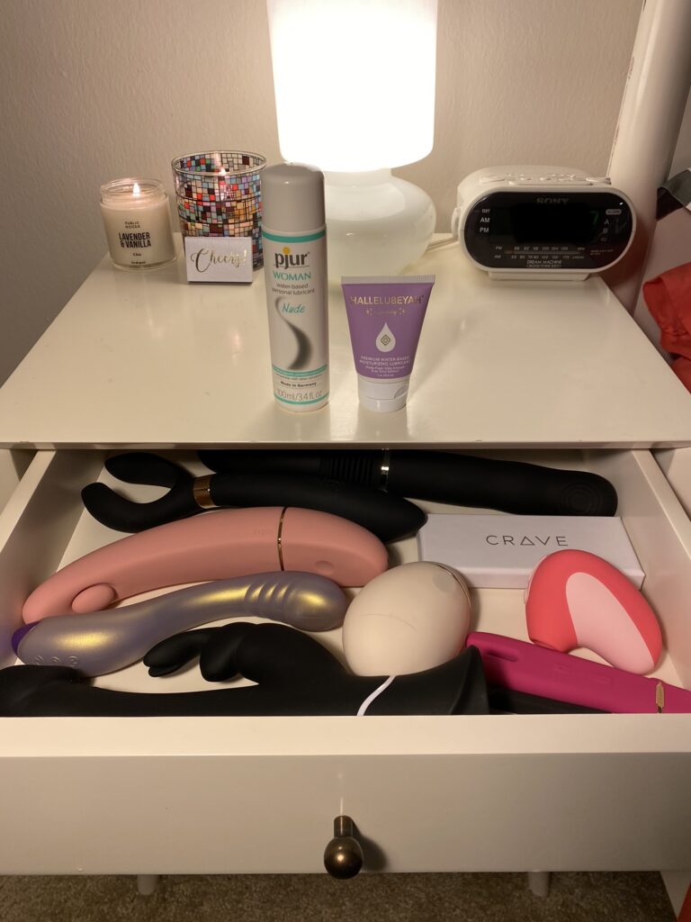 A white nightstand with an open drawer full of vibrators