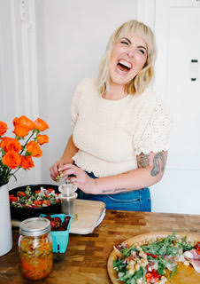 Health coach Anna Jackson at her kitchen counter, making a salad with fresh ingredients, laughing.

