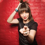 A woman pointing her finger at a red wall.