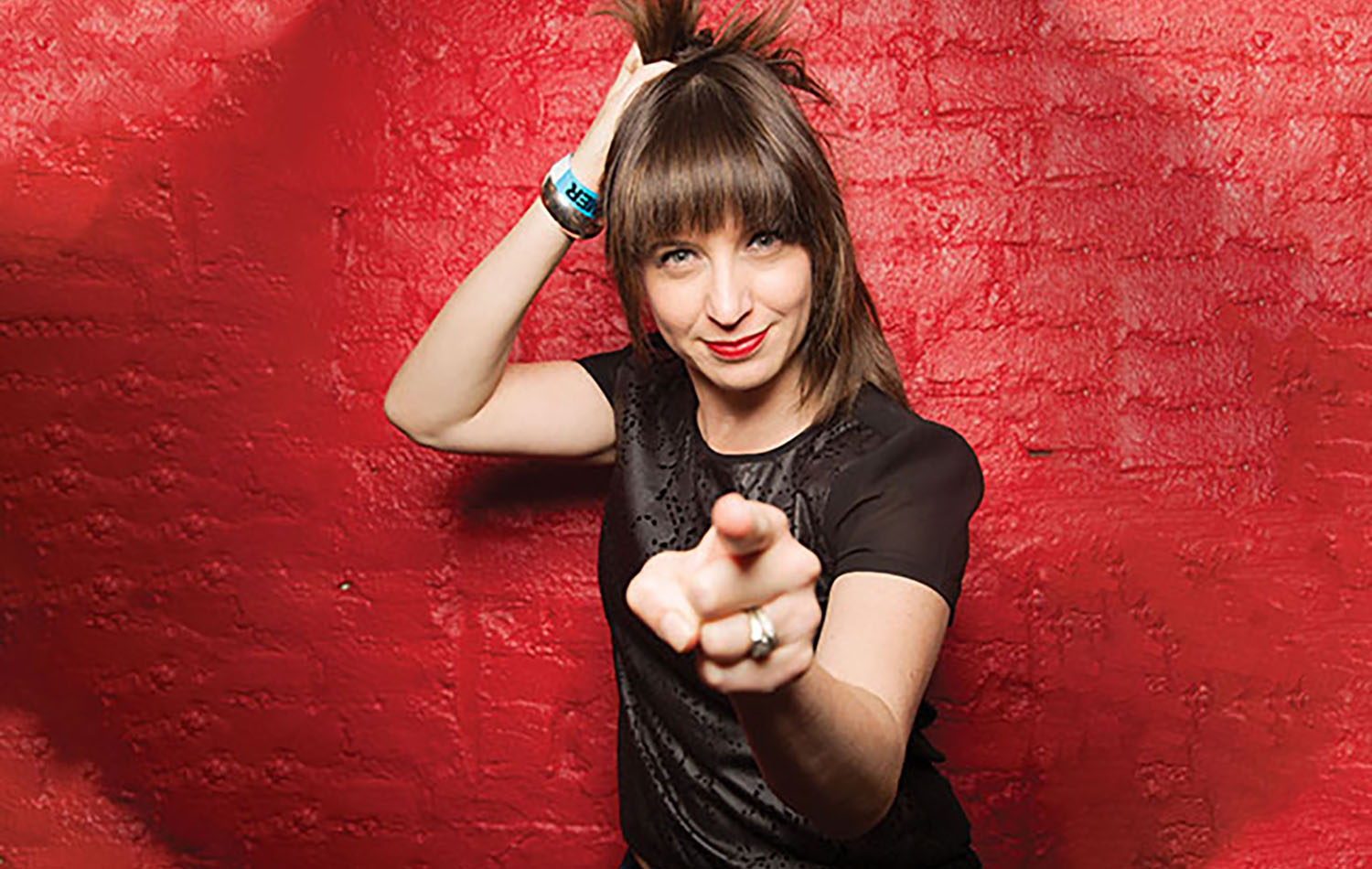 A woman pointing her finger at a red wall.