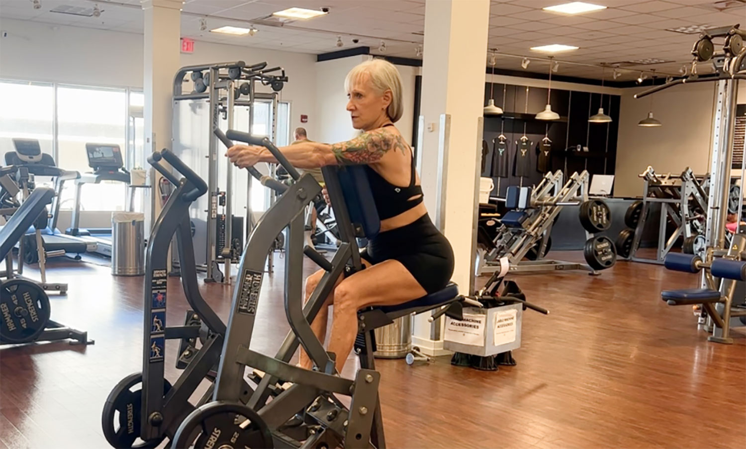 A strong woman is sitting on a stationary bike in a silver gym.
