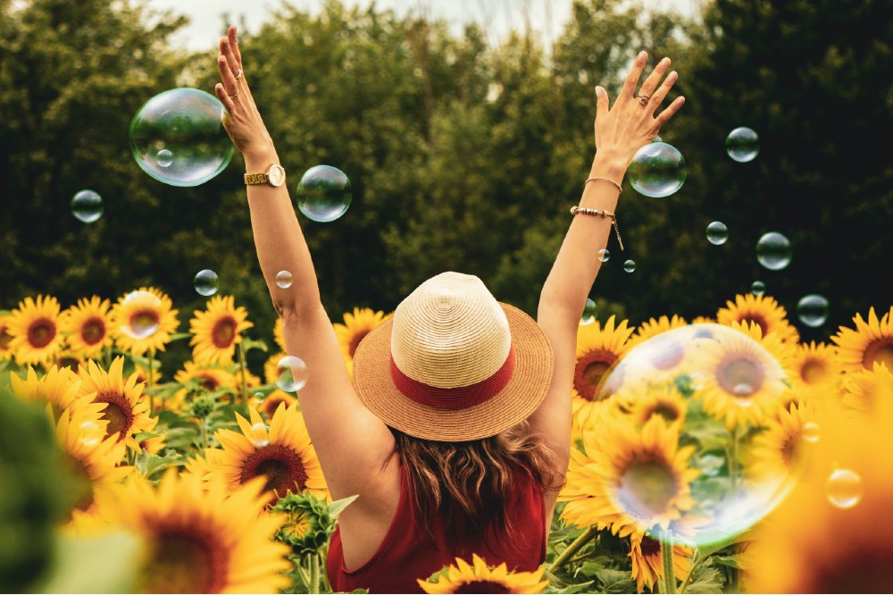 A woman standing in a field of sunflowers with bubbles all around