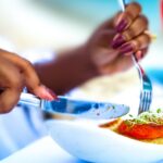 Natural nutrition | A Black woman's hands cutting into a meal on a white plate with a knife.