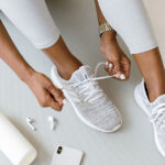 Photo of a woman tying sneakers with a water bottle, phone and ear pods next to her feet