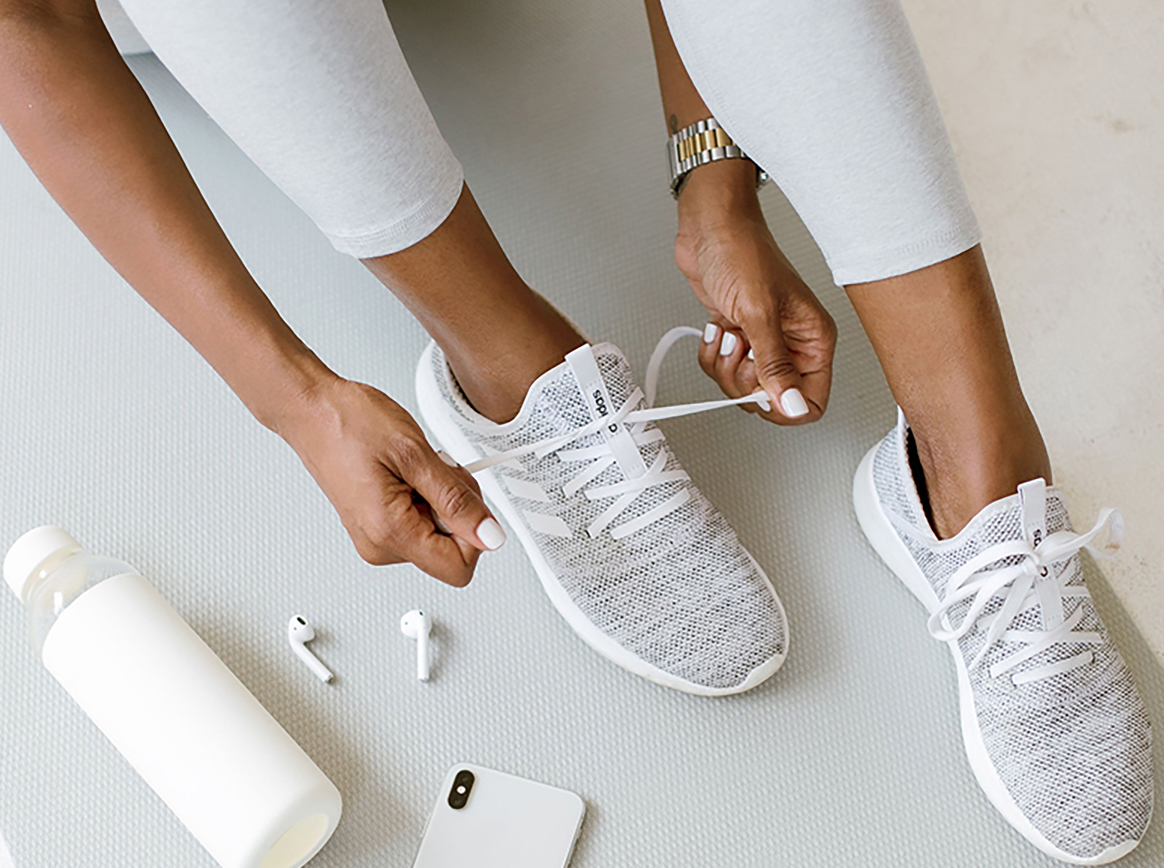 Photo of a woman tying sneakers with a water bottle, phone and ear pods next to her feet
