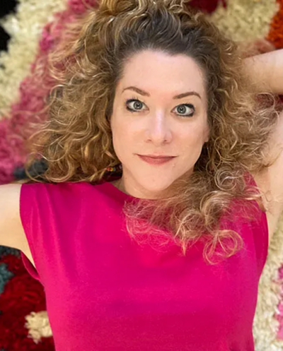 Amy Cuevas Schroeder, a woman with curly hair, is laying on a colorful rug.