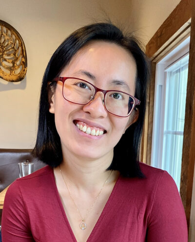 Eve Chen, a woman in glasses, smiling at a table in a restaurant.