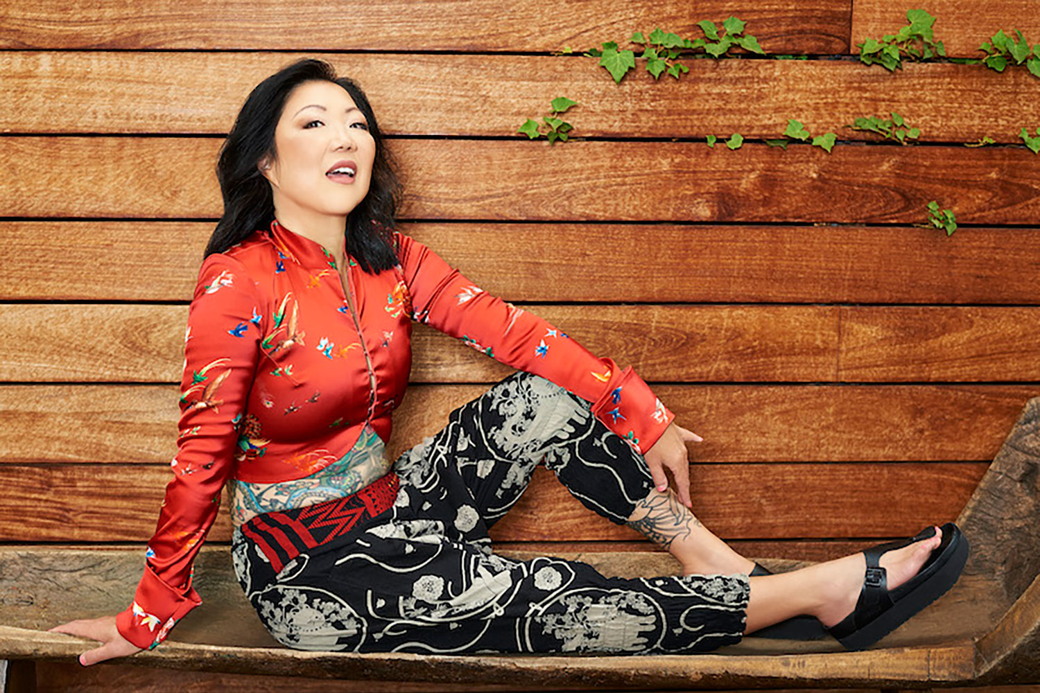 Margaret Cho sitting on a wooden bench during an interview.
