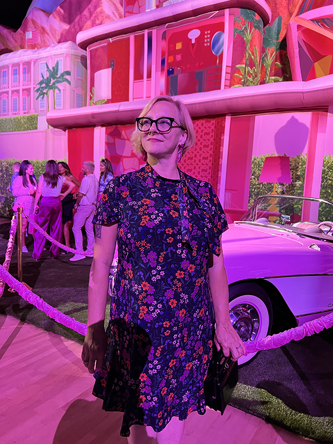 A woman named Sonya Kolowrat wearing a floral dress standing in front of a pink Barbie car.