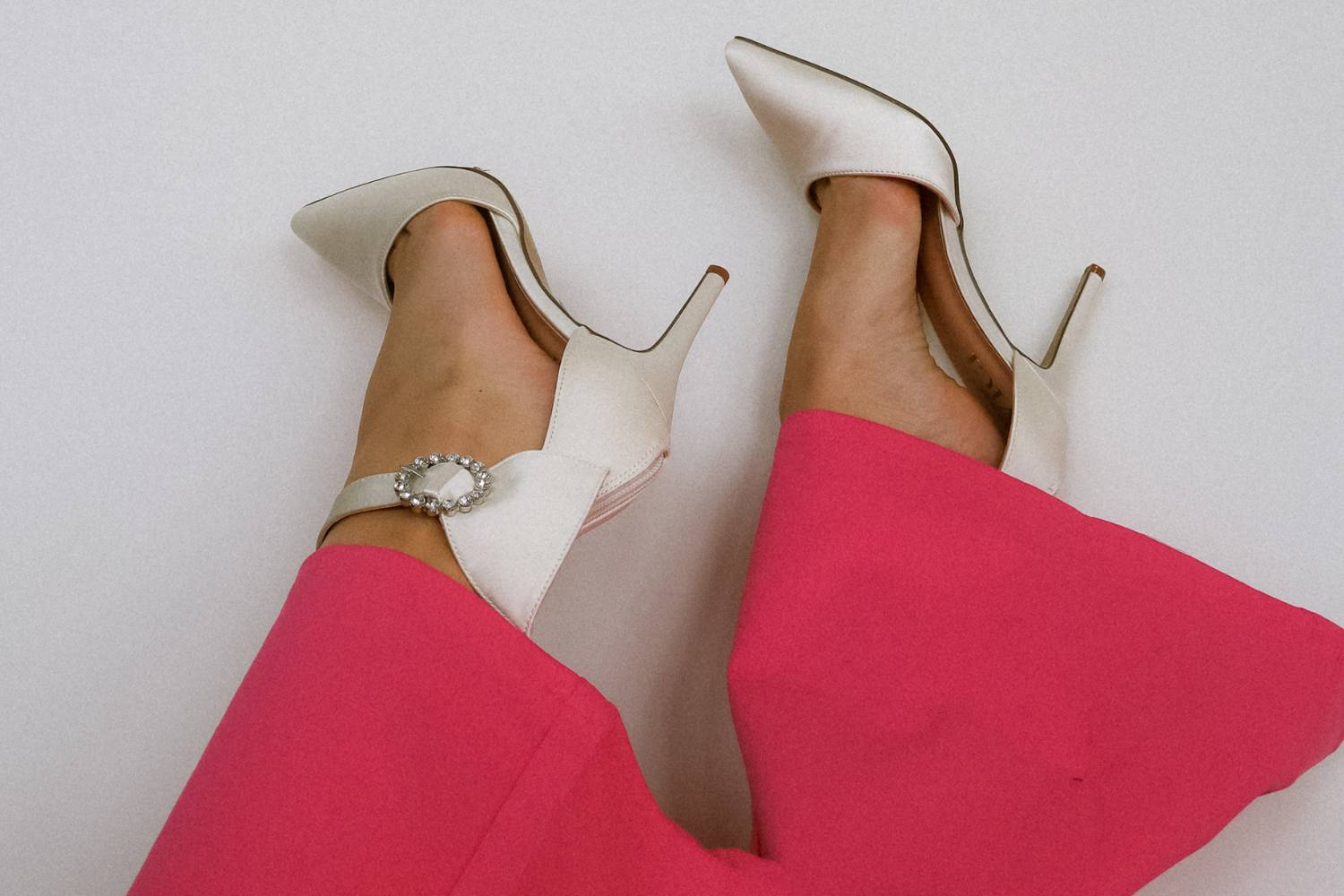 Women's feet in the air wearing white satin heels and hot pink pants