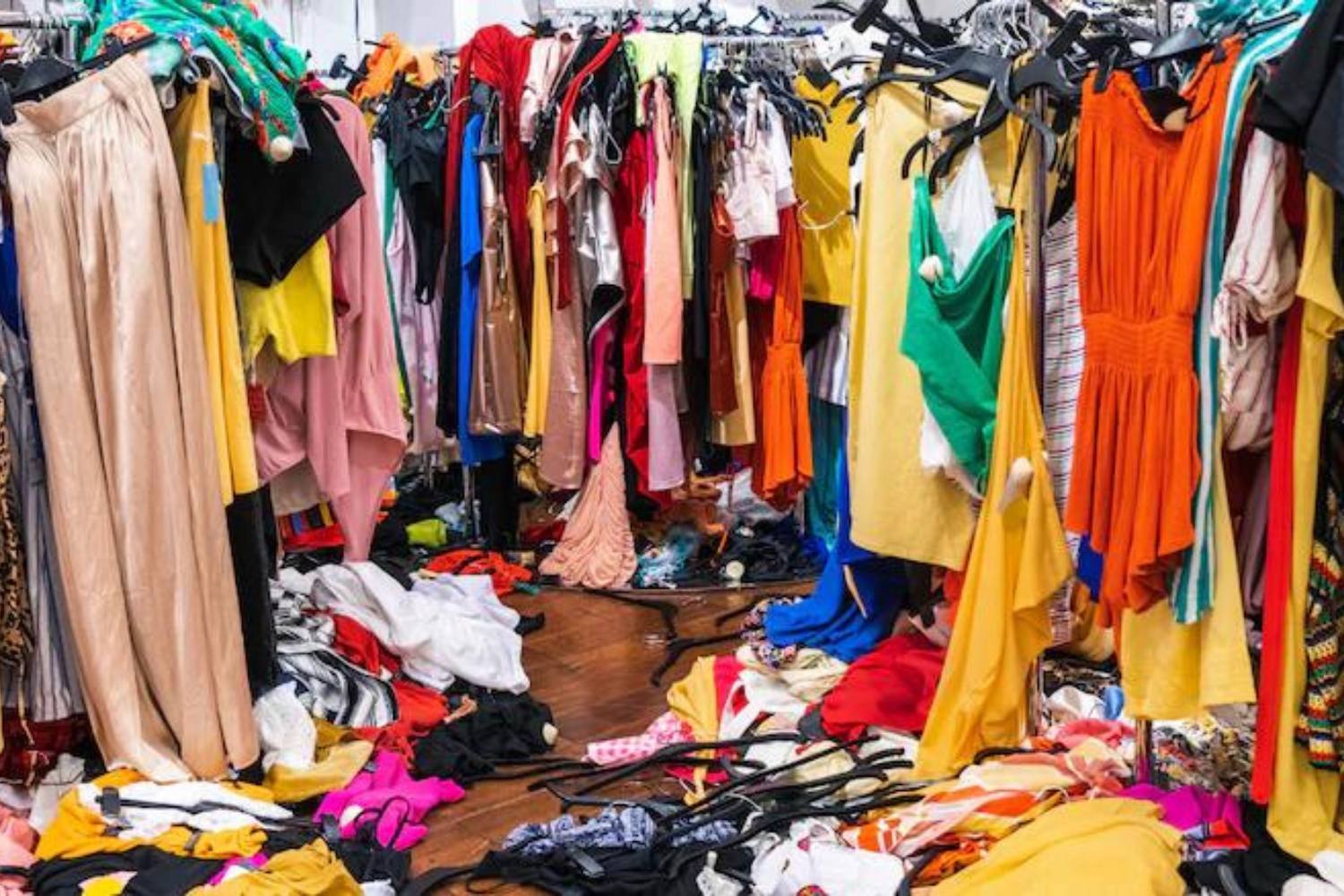 racks of colorful clothing, some fallen as a messy pile on the floor