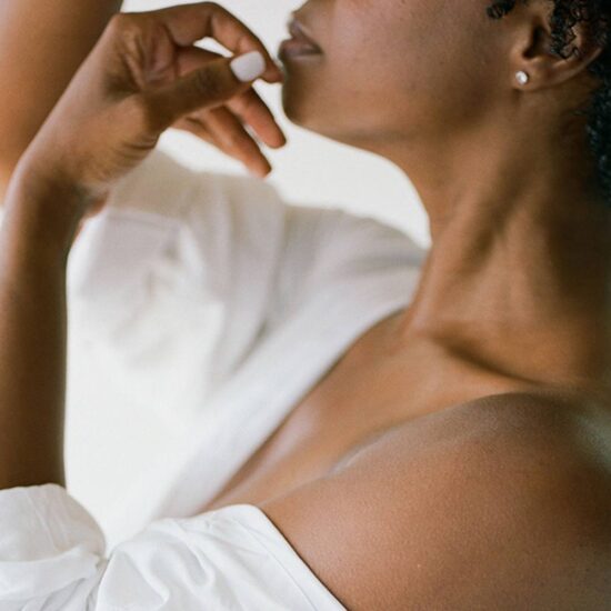 Profile of black woman in white shirt, holding her hands delicately to her face