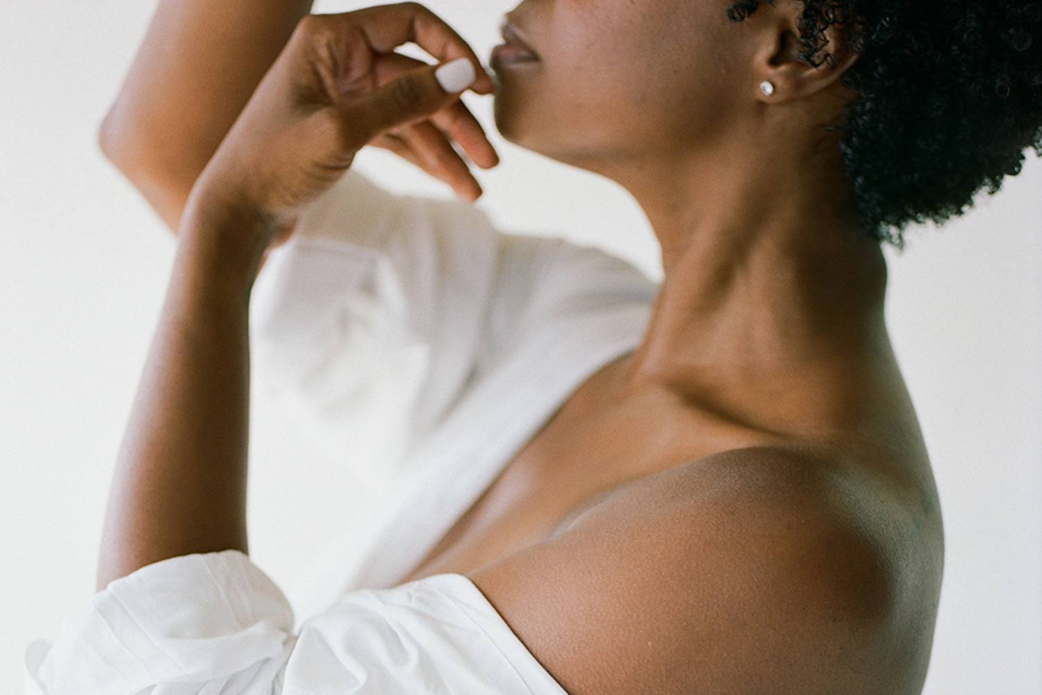 Profile of black woman in white shirt, holding her hands delicately to her face