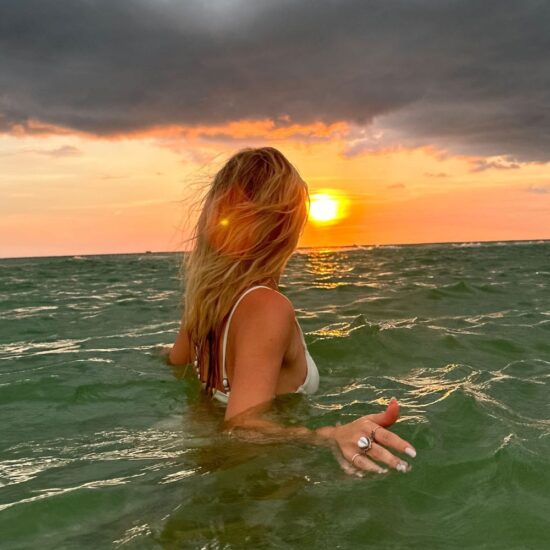 woman in ocean with dark clouds and sun in the horizon