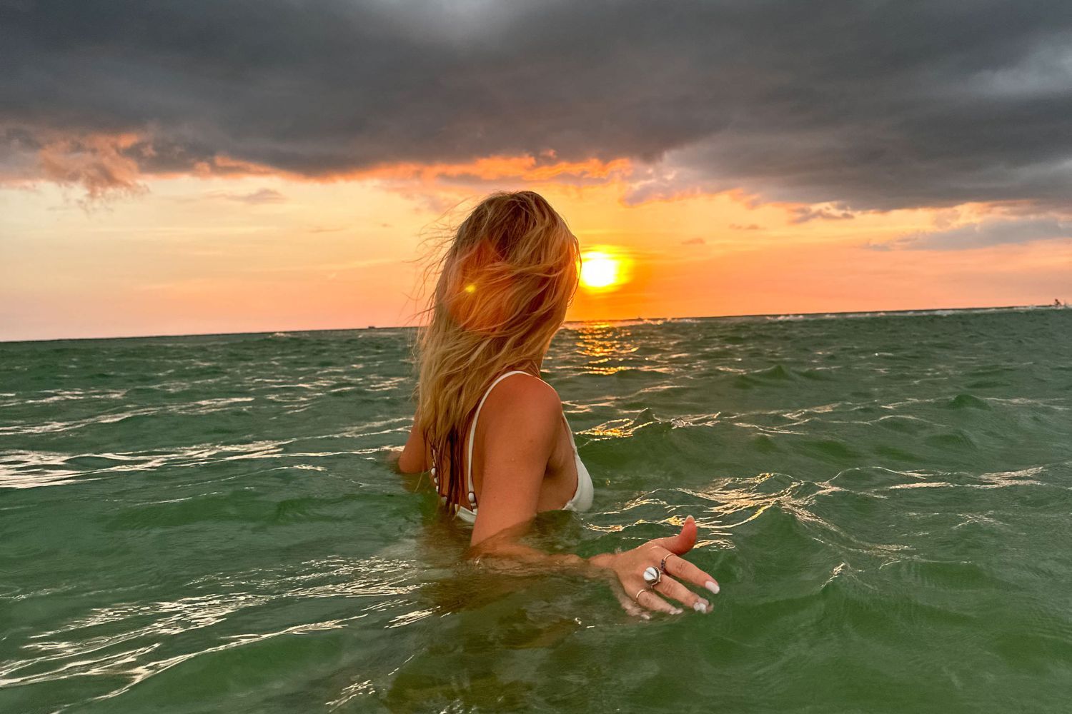 woman in ocean with dark clouds and sun in the horizon