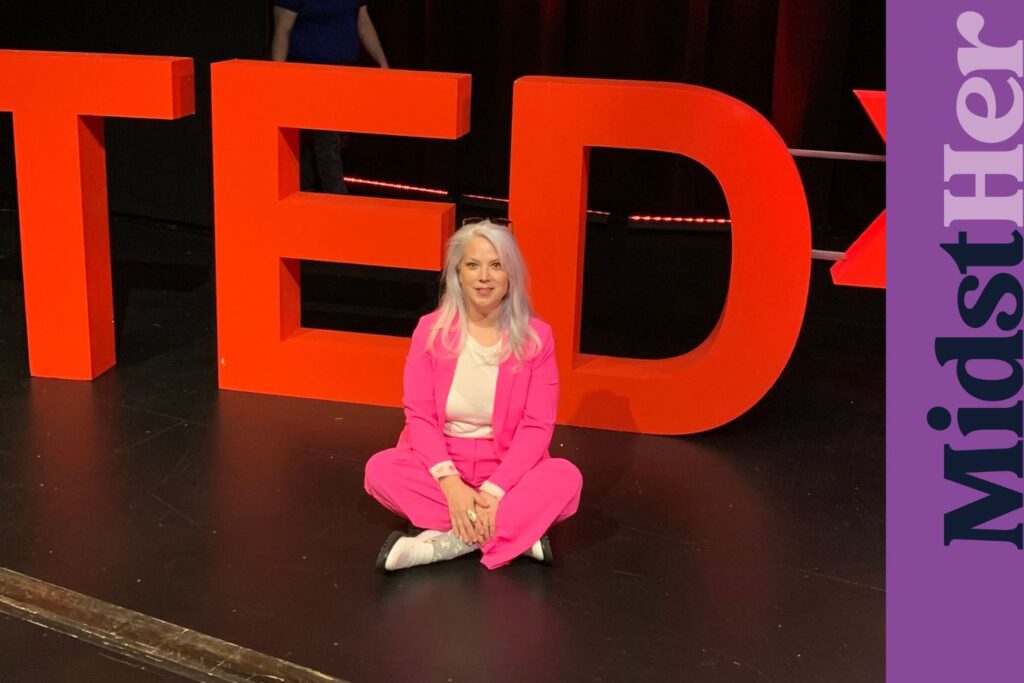 Author Dana Bowman sitting onstage with a TEDx sign behind her