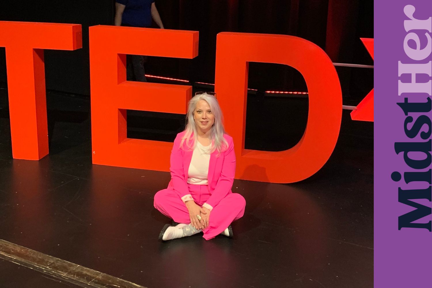 Author Dana Bowman sitting onstage with a TEDx sign behind her