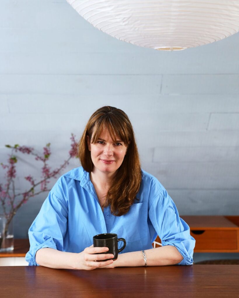 Sarah Coffey sitting at her desk holding a mug