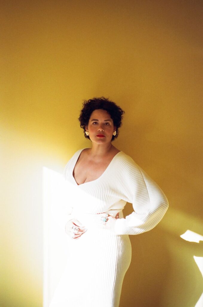 Justina Blakeney portrait. Wearing a white dress. Gold sunny background.